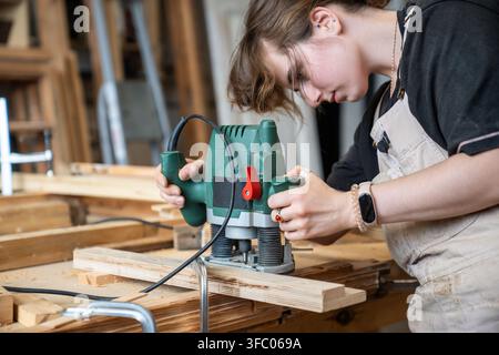 Focused skillful woman restorer working with electric plunge router cutting surface on wooden detail Stock Photo