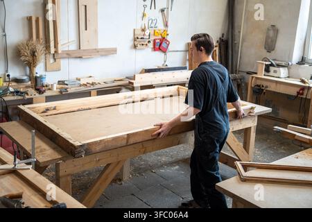 Carpenter preparing wooden window frame for renovation at workbench in carpentry workshop. Stock Photo