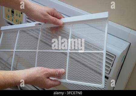 Hands remove a dusty reusable air conditioner filter for cleaning, showing routine HVAC maintenance and household indoor air quality care. Stock Photo