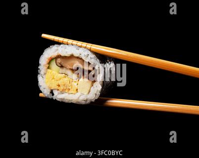 Chopsticks Holding a Piece of Japanese Futomaki Thick Sushi Roll Isolated on Black Background Stock Photo
