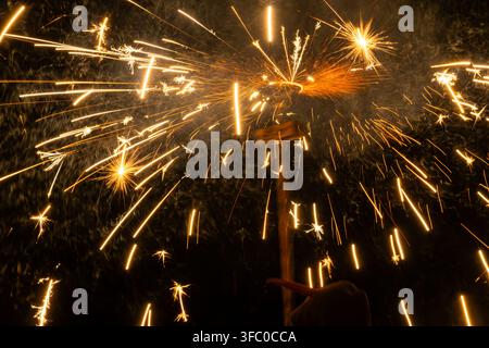 A spinning firework or pyrotechnic device releases an intense burst of golden sparks and glowing fire trails against a dark night background. Long-exp Stock Photo