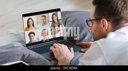Young man having online work meeting on laptop at home, lying in bed and having group video call with his coworkers Stock Photo