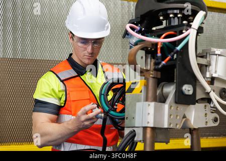 Caucasian male industrial engineer inspecting heavy robot arm machinery and cables in car automobile assembly plant . Power plant factory technician p Stock Photo