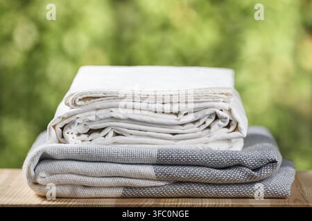 A stack of folded bedding. Monochrome gray white gradient plaid bed sheet textile set on blurred foliage background Stock Photo