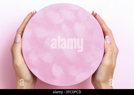 Close-up of female hands holding a large round gift box on a pink pastel background. Birthday valentine's day new year christmas Stock Photo