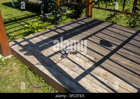 Sunlit wooden deck casts striped shadows from railing. Small animal rests peacefully on weathered planks Stock Photo