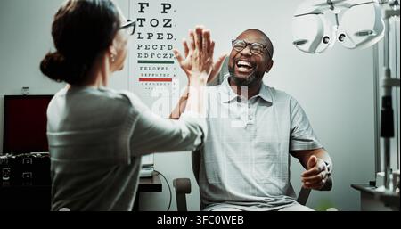 Optometrist, patient and happy with high five for eye care, sight clarity or vision test success. Optometry, worker and mature man in clinic Stock Photo