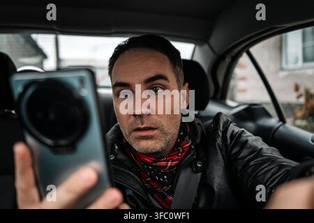 Young driver guy distracted by his phone while in front of the steering wheel, using his smartphone with one hand while driving. Risk and danger situa Stock Photo