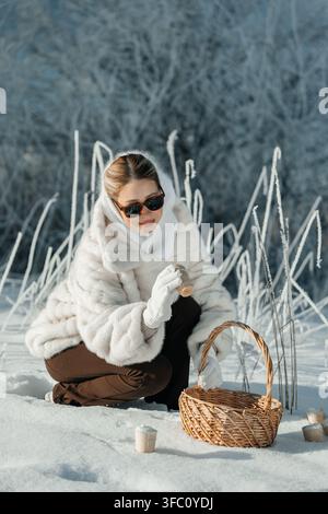 Woman collects items in snowy field in winter season while wearing winter clothes and sunglasses Stock Photo