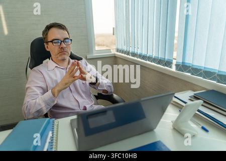 Businessman sitting at his office desk with his hands clasped in front of him, looking thoughtful and serious. Business meeting, waiting, or consideri Stock Photo