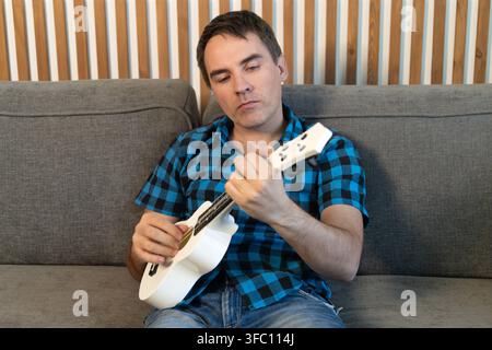 Man sitting on sofa learning to play ukulele, musical hobby and home practice. Stock Photo