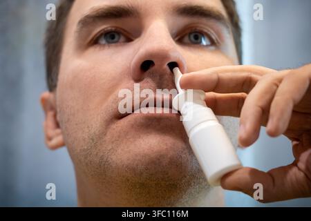 Man using a nasal spray to treat a stuffy nose and congestion, looking at the camera. Allergy relief, sinus treatment, and cold symptoms. Stock Photo