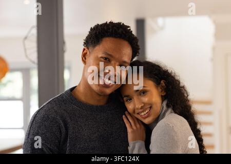African American couple standing close together in home living area, showing sweaters, staircase Stock Photo