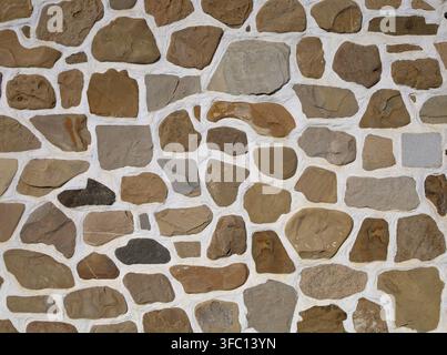 Natural stone wall with flat brown and gray rocks assembled in white cement mortar. Background and texture. Full frame. Stock Photo
