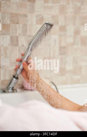 Person's hand holding shower head with water spraying Stock Photo