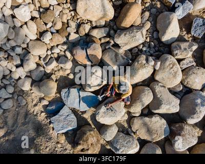 Aerial view of a worker using a hammer and chisel to break large river stones in a quarry in Karanglewas, Central Java, Indonesia. Stock Photo