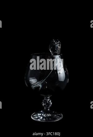 Water spills and creates splashes inside a clear glass sitting on a black surface in this scene of a simple action. Stock Photo