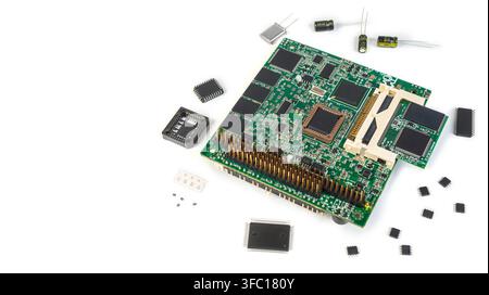 A circuit board is shown with various electronic parts placed around it on a white surface. The components include chips and capacitors. Stock Photo