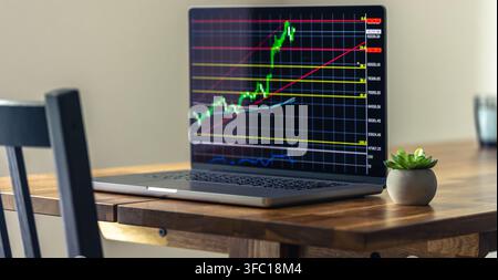 Laptop displaying rising market chart on table. Finance and investment workspace content. Stock Photo