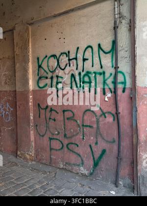 A close-up shot of an aged, textured wall in £ódŸ, Poland, featuring faded two-tone paint (cream and reddish-brown) and vibrant green spray-painted Po Stock Photo