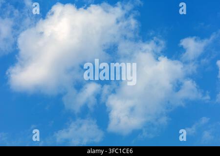Fluffy white clouds float gently across a bright blue sky on a clear day in Spain. Stock Photo