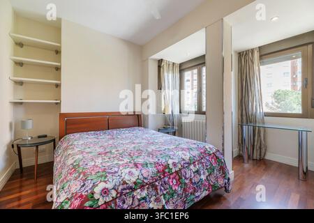 Same floral bedroom viewed from a different angle, showing built-in shelving, mirrored panels, and glass side tables with lamp. Stock Photo