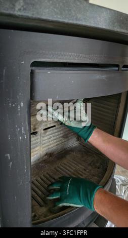 Nussdorf, Germany - November 01, 2025. Hands in protective gloves repairing or replacing a deflector plate inside a wood stove fireplace. Stock Photo