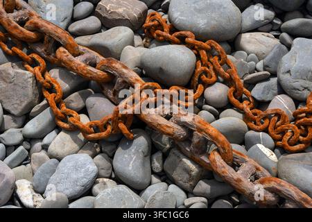 Closeup of old rusty iron links of a chain on a pebble beach for use as a background Stock Photo