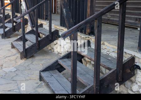 A row of identical dark wooden staircases with simple handrails leading up to a raised stone platform along a textured flagstone pedestrian walkway. Stock Photo