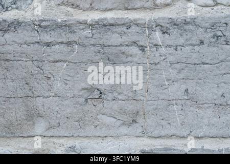 Aged gray masonry wall with rough rectangular stone block. Cracks and weathered surface. Architectural background Stock Photo