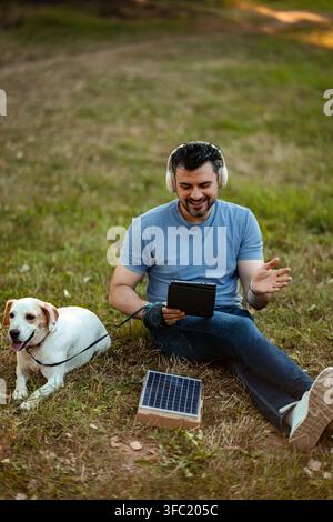 Man and dog relaxing in park, using solar power to charge tablet Stock Photo