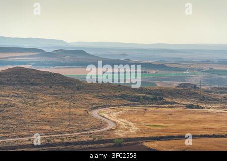 View of a winding dirt road curving through dry agricultural fields and rolling hills near Alcaniz. Teruel, Aragon, Spain Stock Photo