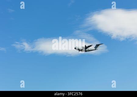 Flying and moving grey military transport aircraft, aeroplane, aeroplane and plane. Blue sky as white clouds. Composition with large negative space an Stock Photo