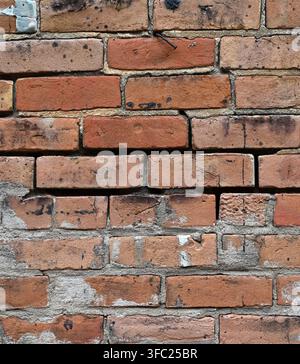Vertical close-up view of a weather-beaten red brick wall surface with worn cracked broken bricks, some discolored Stock Photo