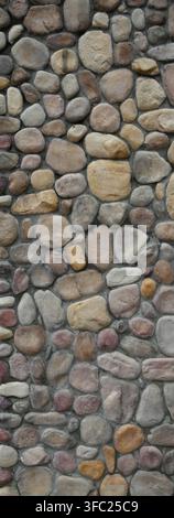 Vertical view of large river rock and mortar wall surface with rounded stones in mixed colors, porous, uneven texture, weathered mortar joints Stock Photo