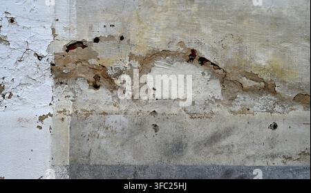 Damaged multi color painted concrete wall surface with weathered cement with flaking holes exposing red brick Stock Photo