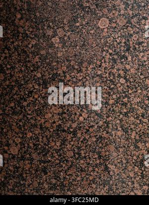 Vertical close up of a polished reddish brown granite surface with black splotches, crater‑like circular patches, gray mottled areas Stock Photo