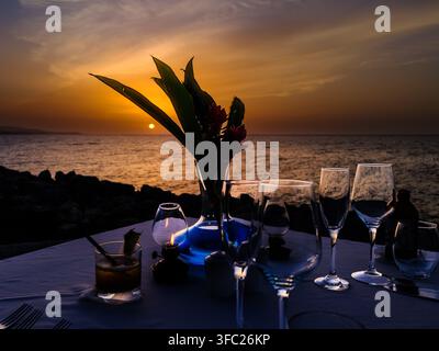 Close-up of a private dinner table set at sunset beside the Caribbean Sea at GoldenEye resort, Oracabessa, Jamaica, with wine glasses, a cocktail, flo Stock Photo