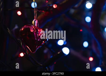 Glass heart ornament hanging among colorful decorative lights creating a festive bokeh background Stock Photo