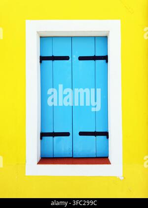 Minimalist blue wooden window shutters on bright yellow wall Stock Photo