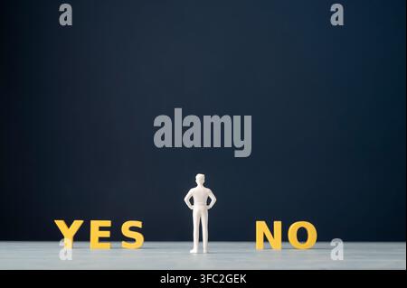 Decision making and choice concept with a businessman figurine standing between yellow YES and NO letters on a dark blue background with copy space. S Stock Photo
