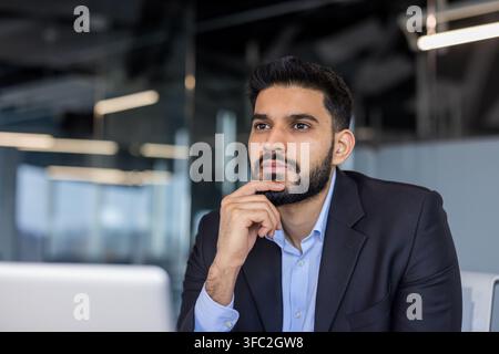 Young male professional concentrating, pondering ideas, and focusing on a business strategy, reflecting determination and ambition in a contemporary workspace Stock Photo