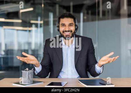 Smiling male customer support agent wearing headset in modern office, offering friendly advice and remote assistance during a video call, confident and professional communicator Stock Photo