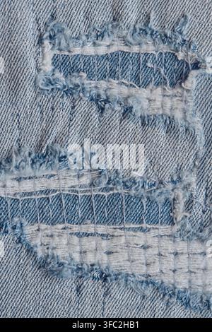 Vertical close up view light blue ripped jeans material with layered white horizontal frayed threads Stock Photo