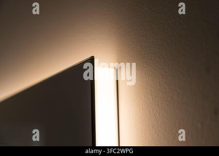 A close-up view showcases the edge of a dark glass panel adjacent to a vertical light source against a textured wall Stock Photo
