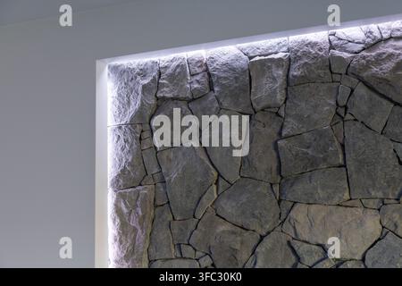A textured stone wall with irregular shaped rocks is illuminated by soft, hidden LED lighting creating a dramatic effect Stock Photo