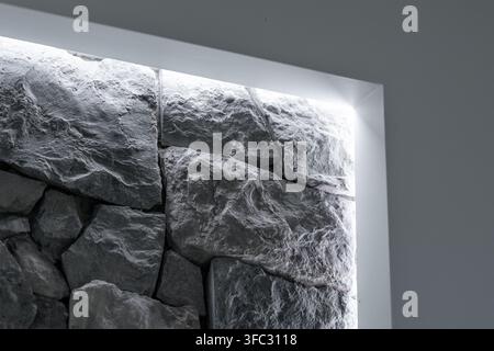 A close-up view of a contemporary stone wall featuring rough-hewn textures illuminated by soft, hidden LED lights creating a dramatic effect Stock Photo