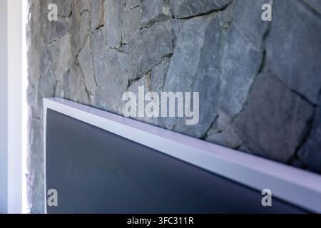 A close-up view showcases a textured slate stone wall behind a contemporary television, highlighting interior design elements Stock Photo