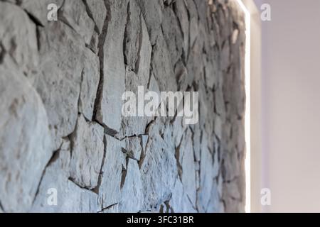 A close-up view of a rough-hewn stone wall surface, showcasing its natural texture and irregular shapes with a soft light illuminating the edge Stock Photo