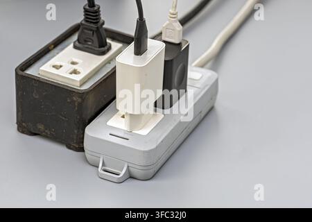 Worn power strip overloaded with multiple chargers and cables, illustrating electrical safety hazards and overload risk. Stock Photo
